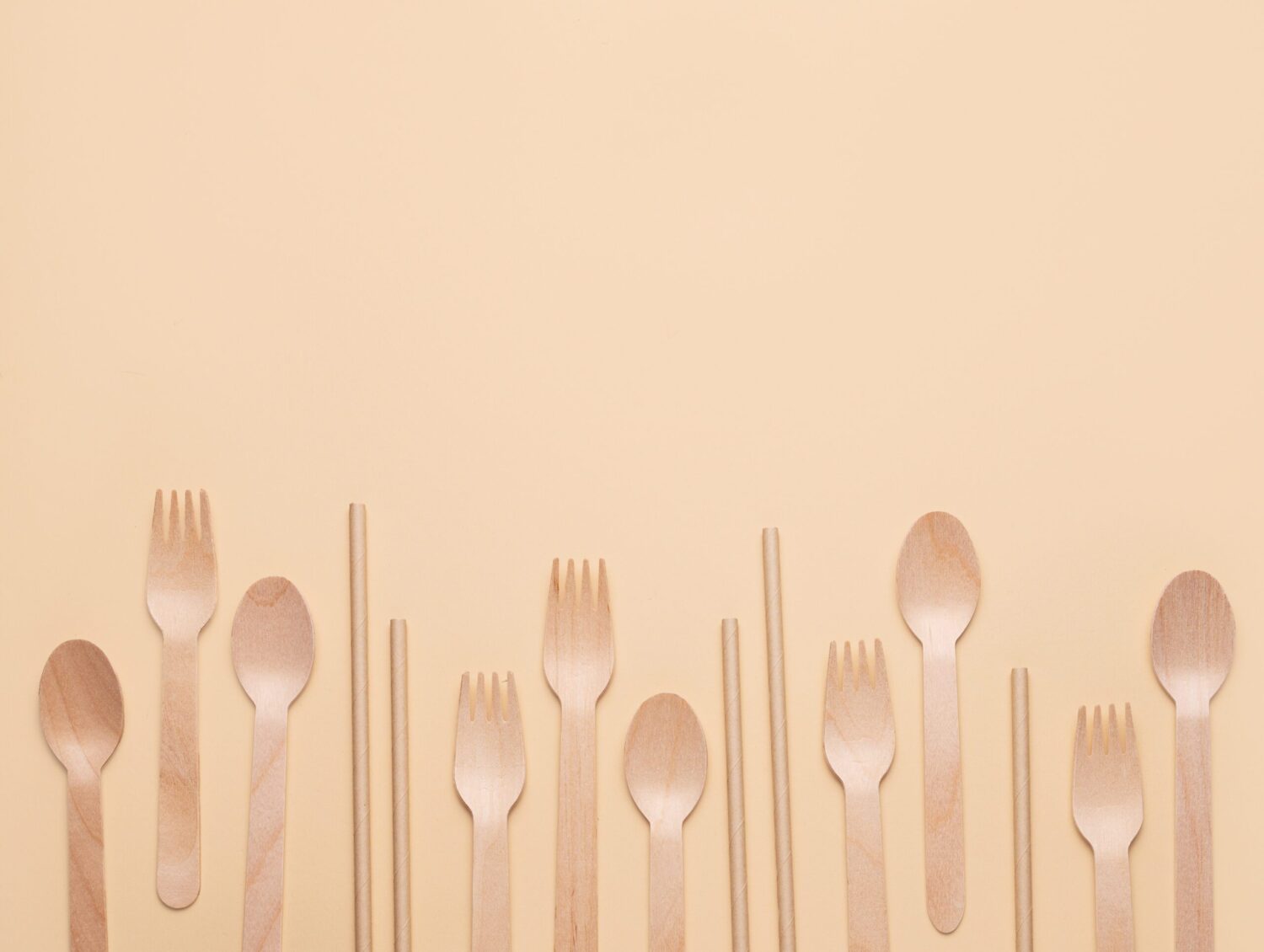 Wooden spoons, forks, and straw arranged in a row on a beige background. Concept of eco-friendly and sustainable kitchen utensils. Top view and copy space.